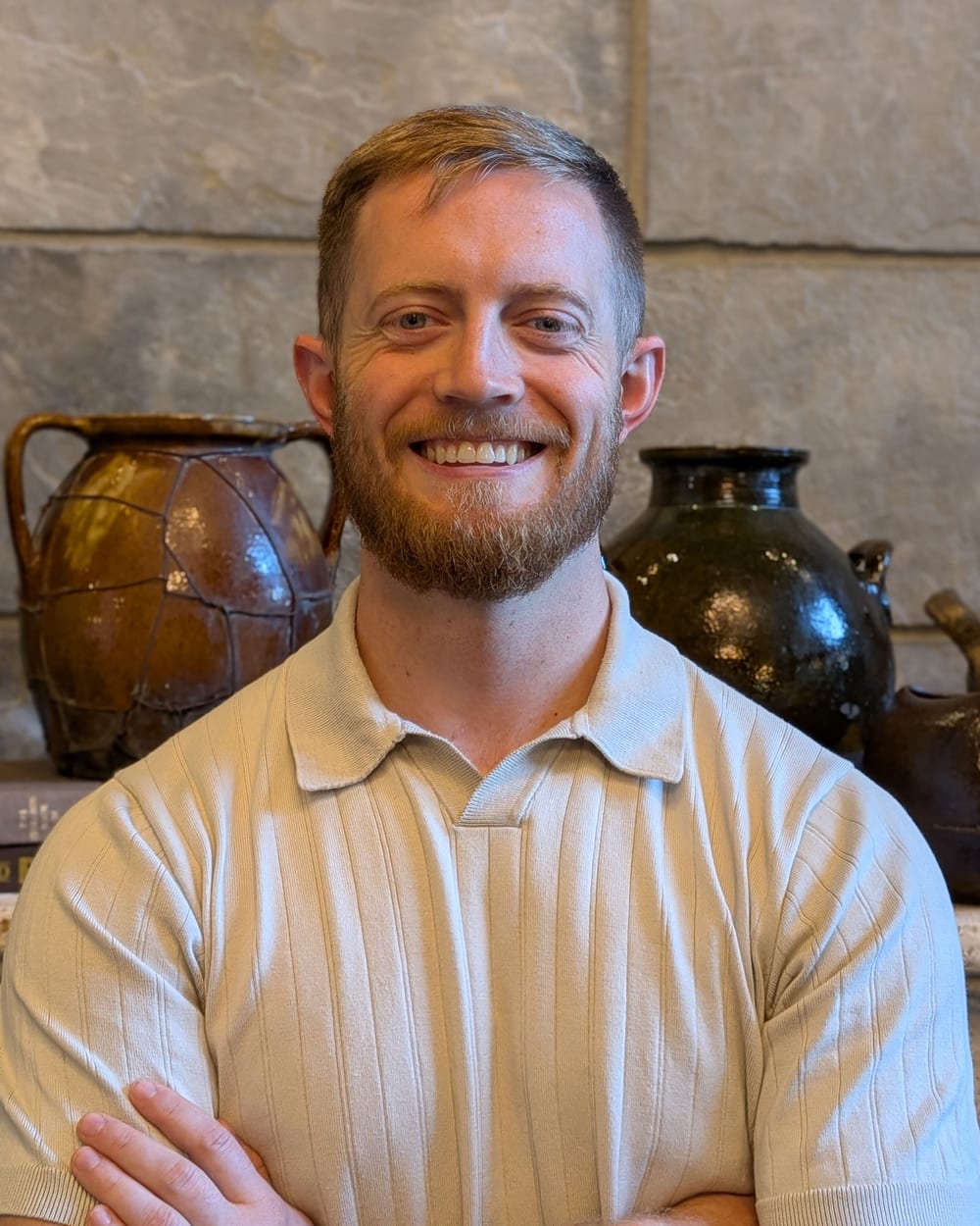 Jonathan Engle smiling with his arms crossed in front of a stone fireplace
