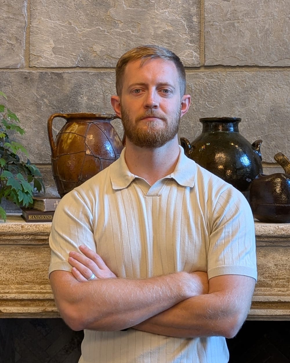 Jonathan Engle standing with his arms crossed in front of a stone mantel lined with pottery
