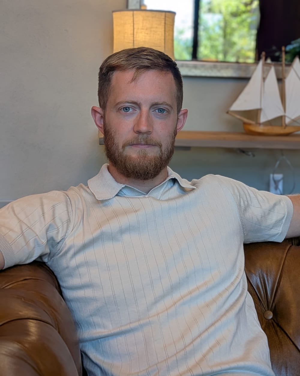 Jonathan Engle seated on a leather sofa, a model sailboat on the shelf behind him