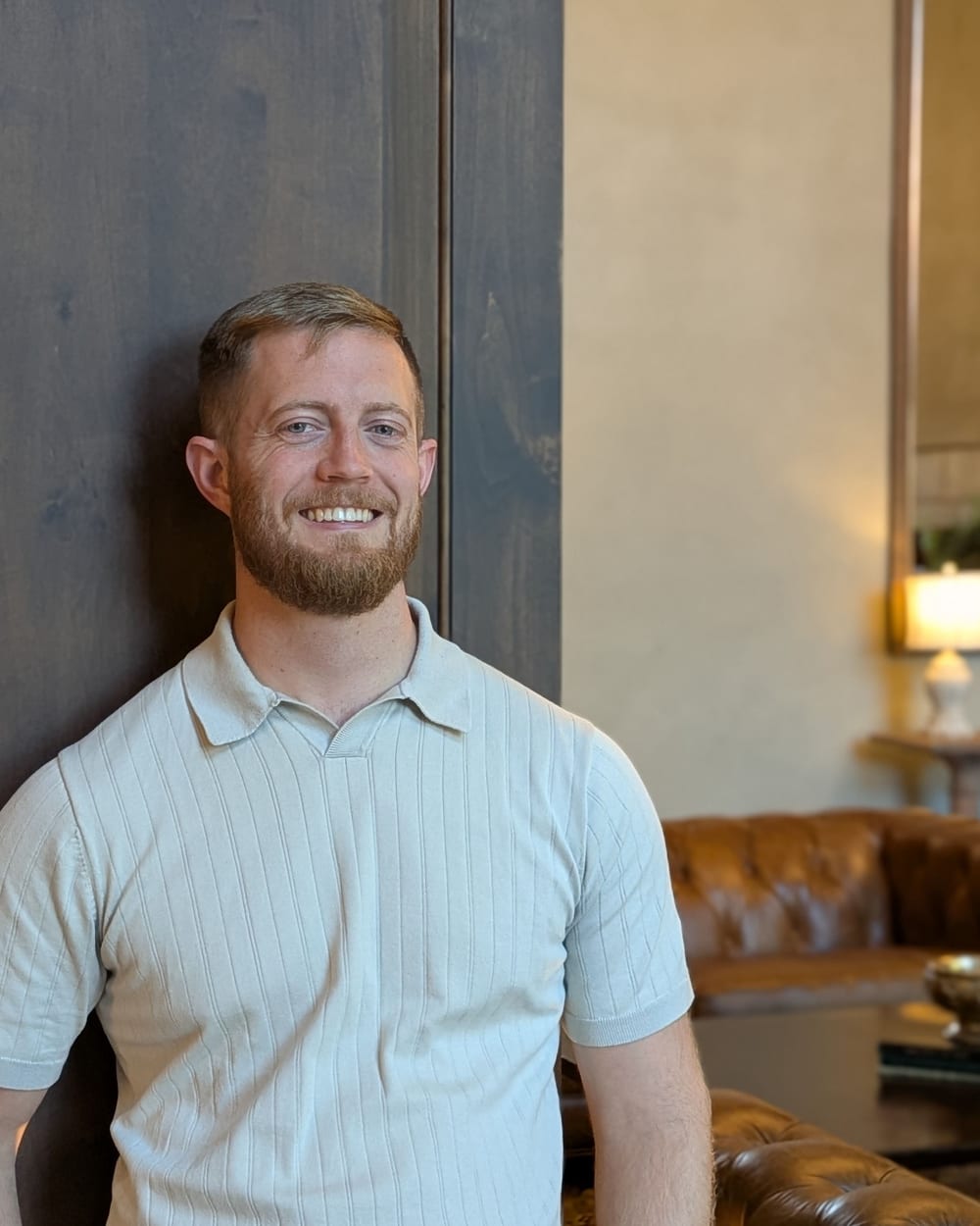 Jonathan Engle smiling in a lounge, a leather sofa and lamp behind him